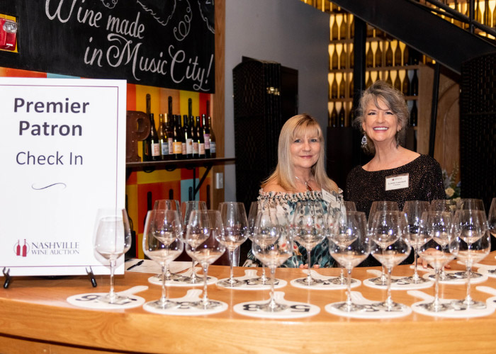 Two women standing at table filled with empty wine glasses