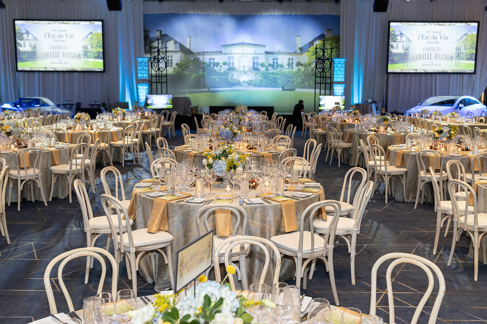 Ballroom set for l'Eté du Vin dinner and auction, tables and chairs in front of a stage.